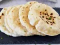 Frisch gebackenes pita brot, leicht gebräunt und mit Petersilie garniert, liegt auf einem dunklen Stein.