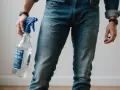 Mężczyzna w dżinsach trzyma butelkę z rozpylaczem, pokazując, jak rozciągnąć spodnie w pasie.
