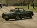 Auto d'epoca verde scuro in movimento, con conducente con cappello. La targa suggerisce che siamo in Inghilterra, dove si guida a destra.