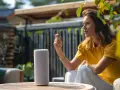 Frau spricht mit einem Smart Speaker im Garten. Sie verbindet ihr Gerät und genießt die Musik.