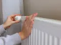 Dłonie regulują termostat grzejnika. Kiedy zakończy się sezon grzewczy w blokach?