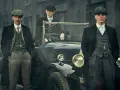 Tre uomini in abiti eleganti, stile Peaky Blinders, posano accanto a un'auto d'epoca.