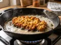 Ein goldbraunes Schnitzel braten in heißem Fett in einer Gusseisenpfanne. Dampf steigt auf, während die Panade knusprig wird.