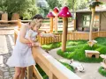 Mutter zeigt Kind im Streichelzoo Berlin ein Kaninchen. Pilz-Deko und Holzhäuschen schaffen märchenhafte Atmosphäre.