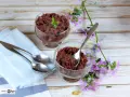 Dos copas de delicioso mousse de chocolate de la abuela, decoradas con menta y flores moradas, listas para disfrutar.