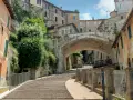 Perugia co zobaczyć: malownicze schody prowadzące pod zabytkowy most, otoczone kamiennymi domami i zielenią.