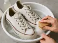 Manos limpian zapatillas blancas con cepillo en agua jabonosa. Aprende como lavar zapatillas blancas y que no queden amarillas.
