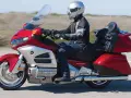 Mężczyzna w kasku jedzie lśniącym, czerwonym motocyklem turystycznym Honda Gold Wing.