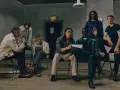 Grupo de hombres con un look business casual, sentados y de pie en una sala con un letrero de "EXIT".