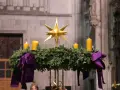 Ein Adventskranz mit vier gelben Kerzen und einem goldenen Stern, geschmückt mit lila Bändern. Seine Bedeutung liegt im Warten und Hoffen auf Weihnachten.