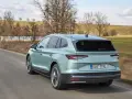 Jasnozielony Skoda Enyaq jedzie po wiejskiej drodze, otoczony wiosennym krajobrazem z drzewami i zielonymi polami.