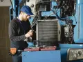 Mechanik w niebieskiej czapce i kombinezonie naprawia ciężarówkę, trzymając narzędzie.