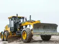 Żółta równiarka do ciągnika pracuje na błotnistym placu budowy, wyrównując teren.