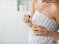 Frau mit Handtuch hält Pipettenflasche mit goldenem Öl. Ein Schritt in der Hautpflege in der Pflege für strahlende Haut.