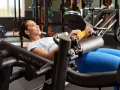 Femme souriante effectuant un hip thrust sur une machine de musculation, concentrée sur son entraînement.