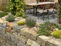 Natürliche Steinmauer mit Kräutern und Blumen, die schöne Ideen für den Garten bietet. Eine Sitzgruppe lädt zum Verweilen ein.