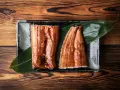 Dwa kawałki glazurowanego węgorza do sushi, podane na liściu na ciemnej zastawie, na drewnianym tle.