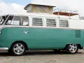 En turkos och vit volkswagen folkabuss med taklucka och takräcke står på en sandstrand.