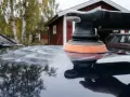 Polermaskin med skumrondell skapar virvlar på bilens lack. I bakgrunden syns ett rött hus och en äldre bil.