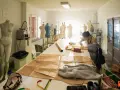 Dans un atelier d'une école d'arts, une jeune femme coupe du tissu sur une grande table. Des mannequins et du matériel de couture sont visibles.