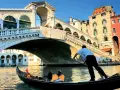 Gondola sotto il Ponte di Rialto, un'icona delle piazze Venezia, con edifici colorati e turisti che ammirano il panorama.