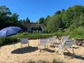 Sonnige Tage am Stedener See: Liegestühle und Sonnenschirm warten auf Besucher vor einem Reetdachhaus.