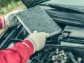 Hands in gloves hold a dirty cabin air filter, ready for replacement. This contrasts with the engine air filter, unseen but vital for car performance.