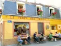 Café "Le Temps des Cerises" con un encantador estilo francés, balcones floridos y gente disfrutando en sus mesas exteriores.