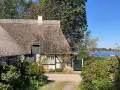 Reetgedecktes Haus am Wasser, ein **damp geheimtipp** mit Booten im Hintergrund.