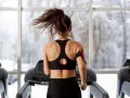 Une femme fait du sport à jeun sur un tapis roulant, ses cheveux flottant au vent. Dehors, la neige tombe.