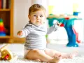 Ein neugieriges 8 Monate altes Baby mit blauen Augen sitzt auf einem flauschigen Teppich und spielt mit Spielzeug.