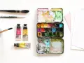 Matériel d'artiste : palette de peinture, tubes de couleur, pinceaux et papier pour le support aquarelle.