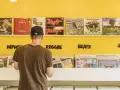 Mann durchstöbert Schallplatten in einem bunten Plattenladen in Berlin. Musikgenres wie HipHop, Reggae, Beatz und Jazz sind angeschrieben.