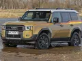 Złoty Toyota Land Cruiser Prado z kolorowymi pasami na boku, wjeżdża do wody.