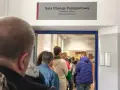 Kolejka do sali obsługi paszportowej. Czy odbiór paszportu musi być osobiście? Ludzie czekają w środku i na zewnątrz.