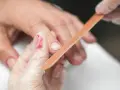 Dłoń w rękawiczce kosmetycznej jest piłowana pilnikiem, przygotowując paznokcie do nałożenia hybrydy.