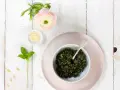 Schüssel mit frischem Basilikum-Pesto, Pinienkernen, Parmesan und einer zarten rosa Blume. Ein Hauch des originalrezepts.
