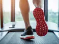 Gambe che corrono su un tapis roulant, con una scarpa rossa e nera in primo piano. Un'ottima immagine per chi vuole capire come iniziare a camminare.
