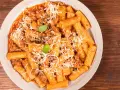 Un piatto invitante di pasta alla zozzona, con rigatoni conditi con un ricco ragù e abbondante parmigiano grattugiato, guarnito con basilico fresco.