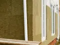 Detalle constructivo SATE: aislamiento de lana mineral en fachada, con ventanas blancas y tubería de desagüe.