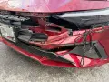 A red car's front bumper is severely damaged, with broken plastic and a rope tied to it. This damage might be from hail, and the owner is likely wondering how do you repair hail damage on a car.