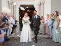 Photographie de mariage : le couple sort de l'église sous une pluie de pétales, entouré de leurs invités joyeux.