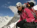 Gerlinde Kaltenbrunner, lächelnd in voller Bergsteigerausrüstung, vor einer majestätischen Schneelandschaft.