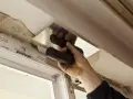 Ręka z kielnią wygładza tynk wokół okna. To etap prac, czym obrobić okna wewnątrz.
