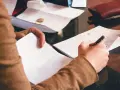 Osoba notuje wydatki, przygotowując się do złożenia wniosku o gwarancję bankową. Na stole leżą rachunki i monety.