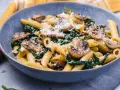 Penne z pieczarkami i szpinakiem, posypane parmezanem, w szarej misce.