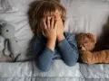 Kind versteckt Gesicht, umgeben von Kuscheltieren. Die Angst um das Kind ist spürbar, es sucht Trost bei seinen Freunden.