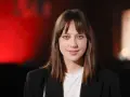 Maria Sobocińska z niebieskimi oczami i grzywką, ubrana w czarną marynarkę i białą koszulkę, uśmiecha się lekko na tle czerwonego światła.
