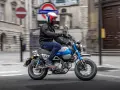 Mężczyzna w kasku jedzie na małym motocyklu, przypominającym boda boda, po ulicy miasta.