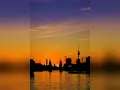 Silhouetten der Berliner Skyline spiegeln sich im Wasser. Ein dramatischer Sonnenuntergang taucht den Himmel in Orange- und Violetttöne.